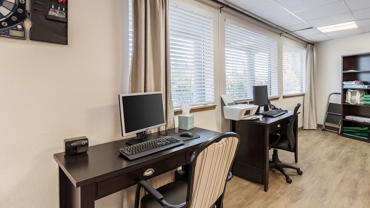 A clean office workspace with computers and desks near large windows.