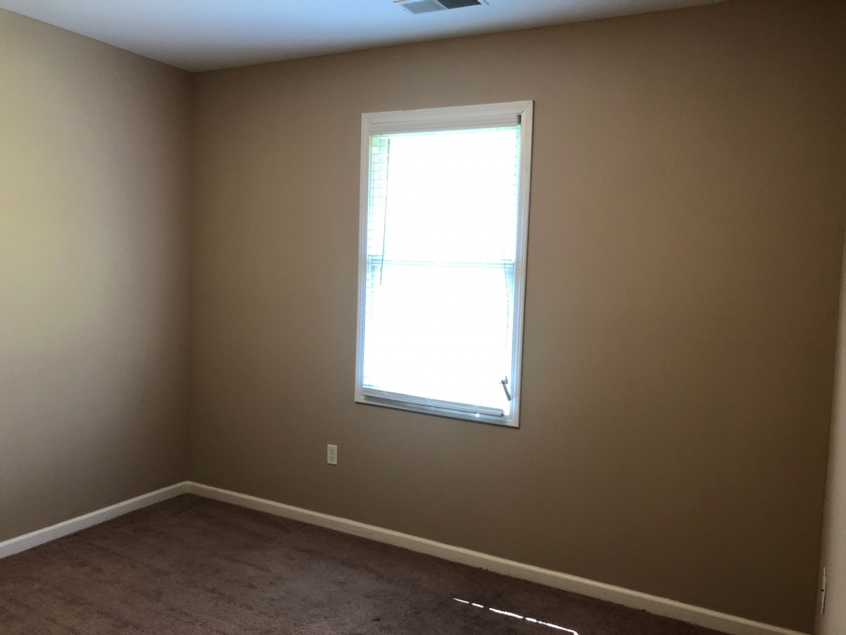 An empty room with beige walls and a single window letting in natural light.