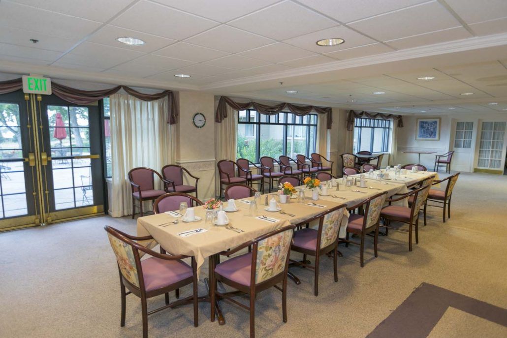 A conference room with a long meeting table surrounded by chairs and large windows with curtains.