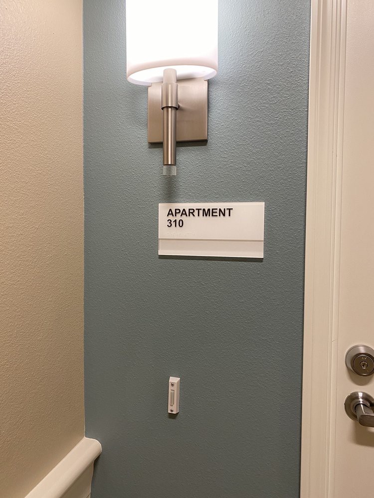 A sign for apartment 316 is mounted on the wall next to a door, illuminated by a wall-mounted light.