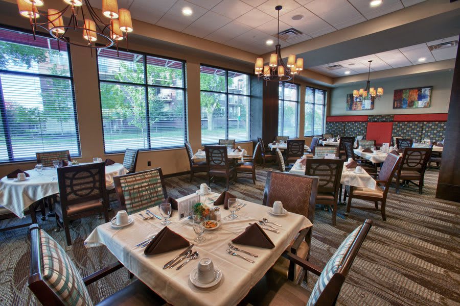 A spacious and elegantly decorated restaurant dining room with neatly set tables and large windows.