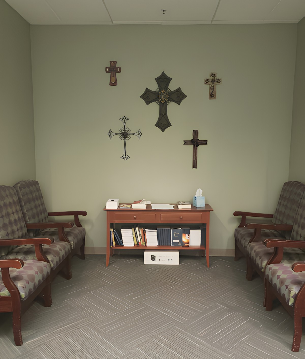 A small waiting room with religious decor including multiple crosses on the wall, two chairs, and a bookshelf with books and a globe.