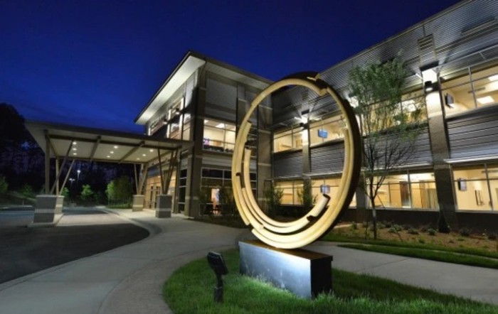 An illuminated sculpture stands in front of a modern building at night.