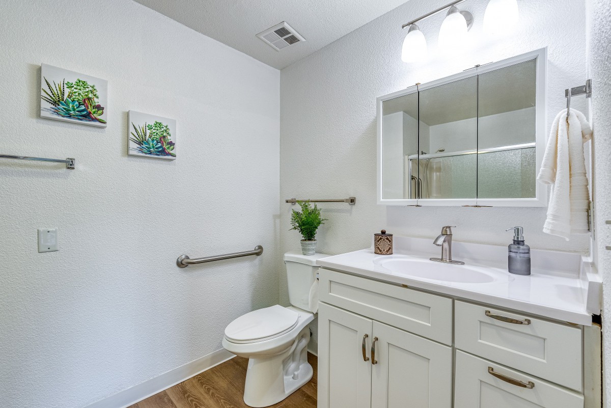 A modern bathroom with light cabinetry, a large mirror, and decorative plants.