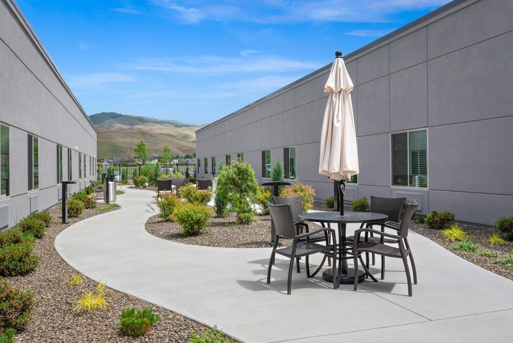 A peaceful outdoor patio area with tables, chairs, and umbrellas surrounded by landscaped gardens.