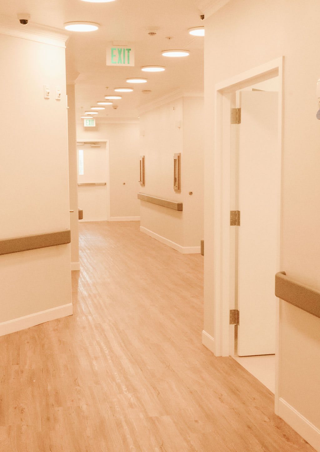 A well-lit, empty hallway in a medical facility with wooden flooring.