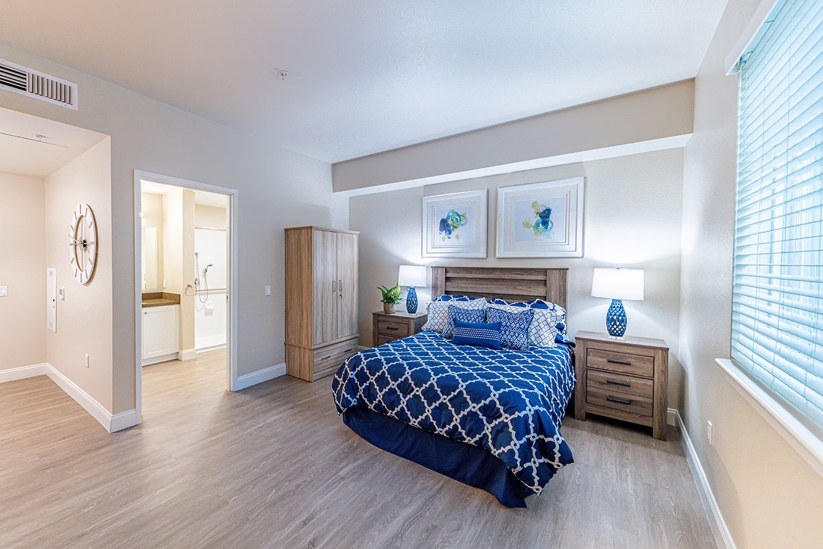 A modern bedroom featuring a double bed with blue patterned bedding, two nightstands with lamps, and a wardrobe.