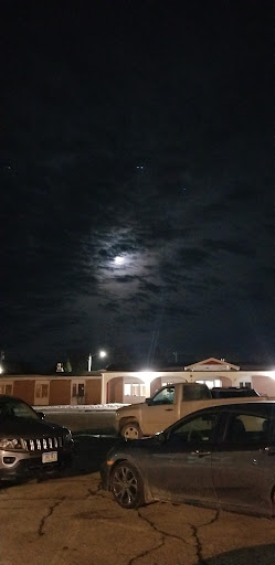 A serene night sky with the moon peeking through the clouds, illuminating nearby buildings.