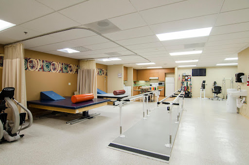A spacious physical therapy room equipped with treatment tables and walking rails.