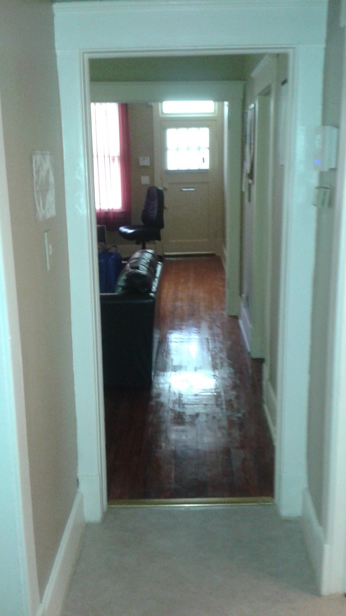 View down a hallway with wooden floors leading to a door.