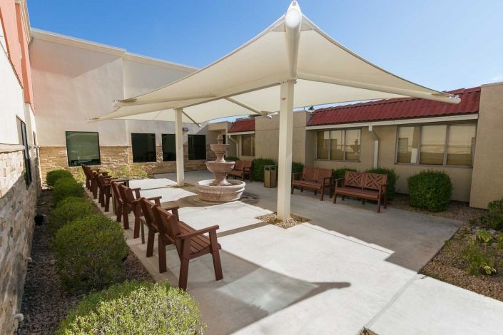 An outdoor patio area with seating under a large shade structure on a sunny day.