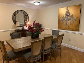 A cozy dining room with a large wooden table, surrounded by chairs, adorned with a floral centerpiece and complemented by wall art and a decorative mirror.