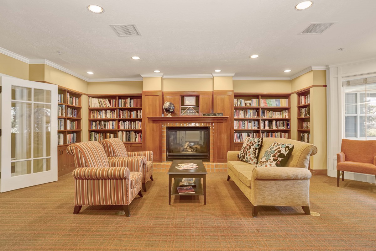 A cozy library with bookshelves, a fireplace, and comfortable seating.