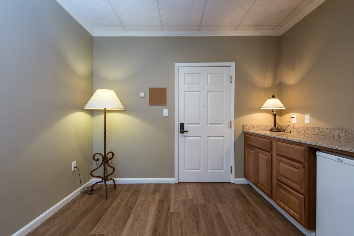 A cozy room with warm lighting, featuring a door, a floor lamp, and a wooden cabinet.