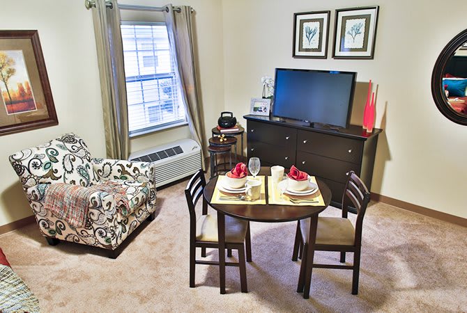 A cozy living room with a small dining table set for two, and a television on a cabinet.