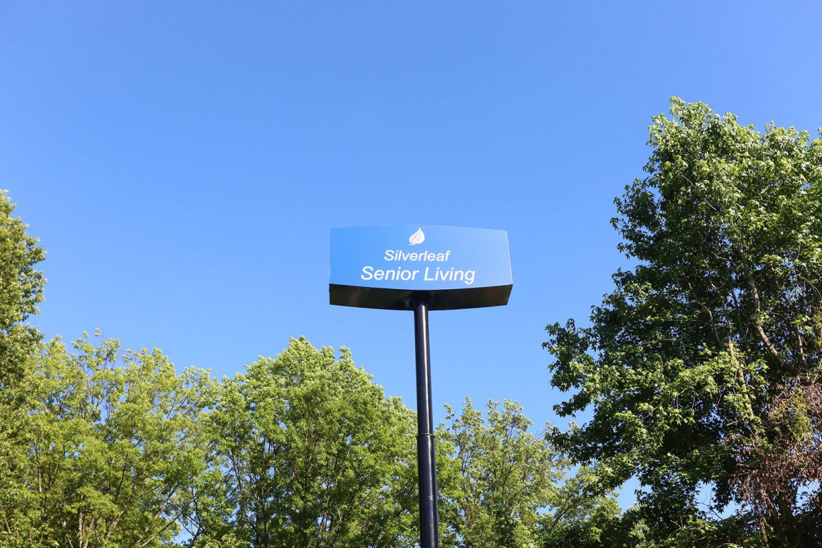A parking sign for senior living against a clear blue sky, surrounded by trees.