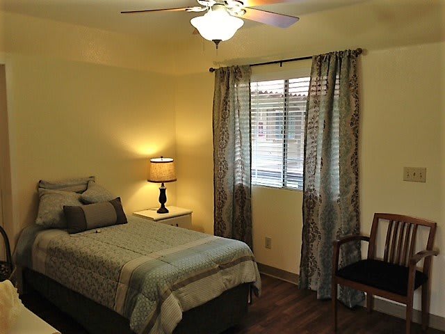 A cozy bedroom with a single bed, lamp, and window with curtains.