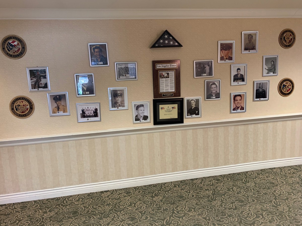 A wall displaying a collection of framed photographs and certificates, arranged around a folded American flag.