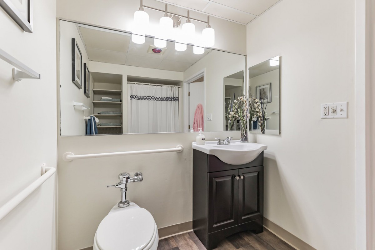 A modern bathroom with a sink, toilet, and large mirror, featuring bright lighting fixtures.