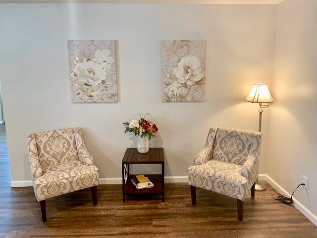 A cozy seating area with two patterned chairs, floral artwork, and a side table with flowers.