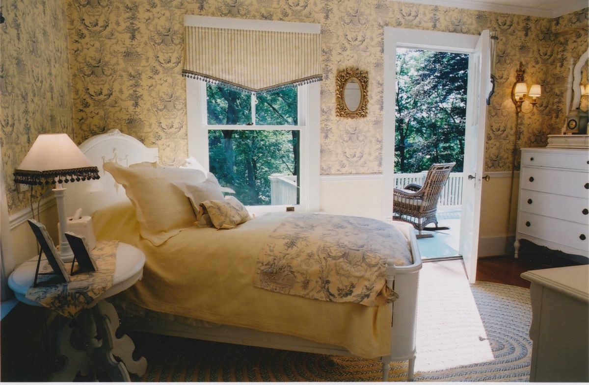 A cozy, traditionally decorated bedroom with a bed near a large window and an open door leading to an outdoor area.