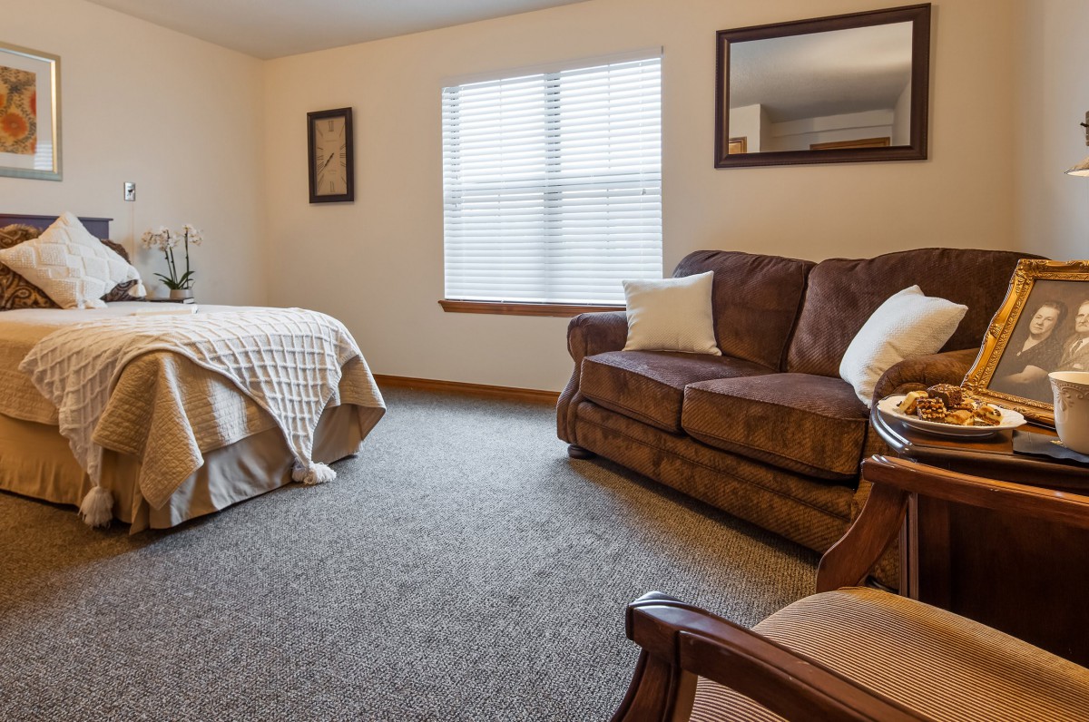 A cozy bedroom with a bed, a sofa, and a window letting in natural light.