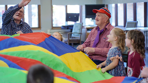 A joyful interaction between children and an elderly man as they play with a colorful parachute.