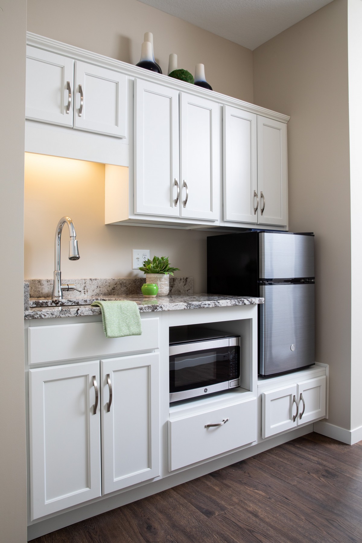 A compact modern kitchen with white cabinets, a small sink, microwave, and refrigerator.