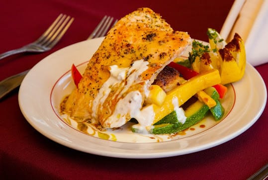 A delicious plate of roasted chicken served with seasoned vegetables and topped with a creamy sauce.