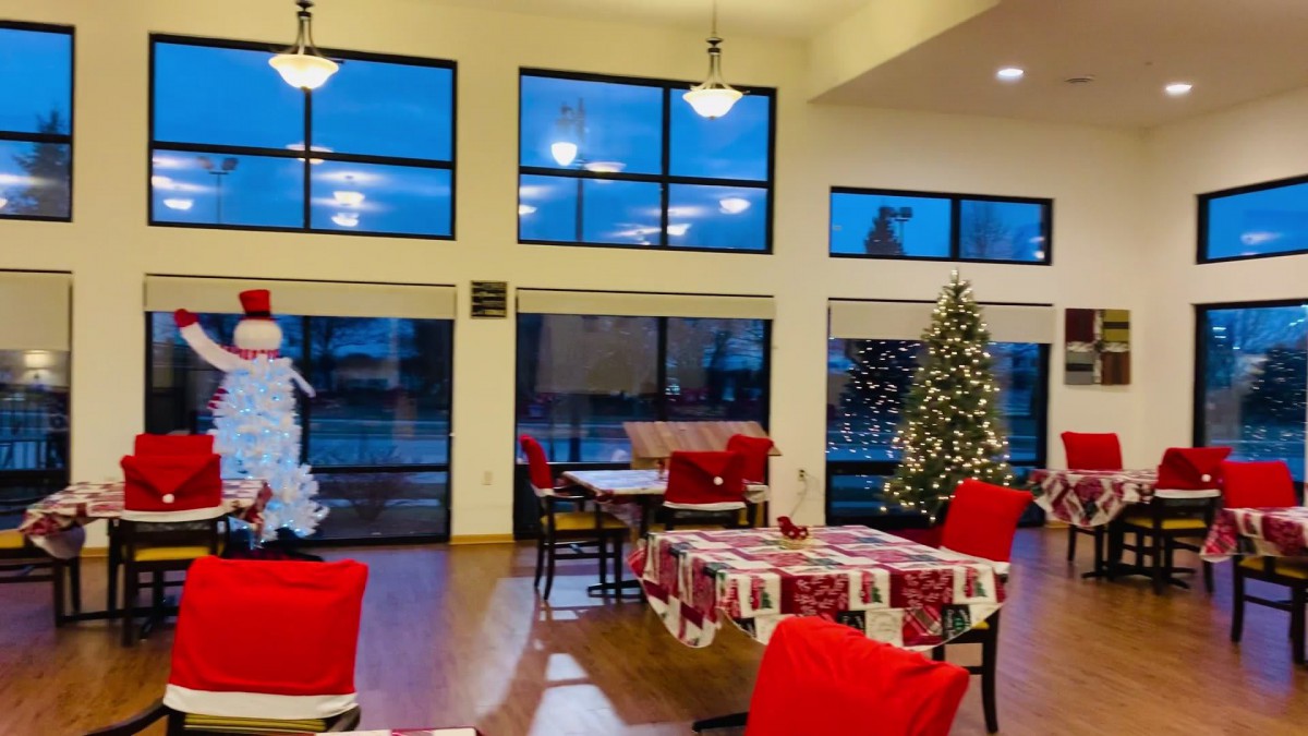 Cozy holiday-themed room with Christmas decorations and a tree by large windows.