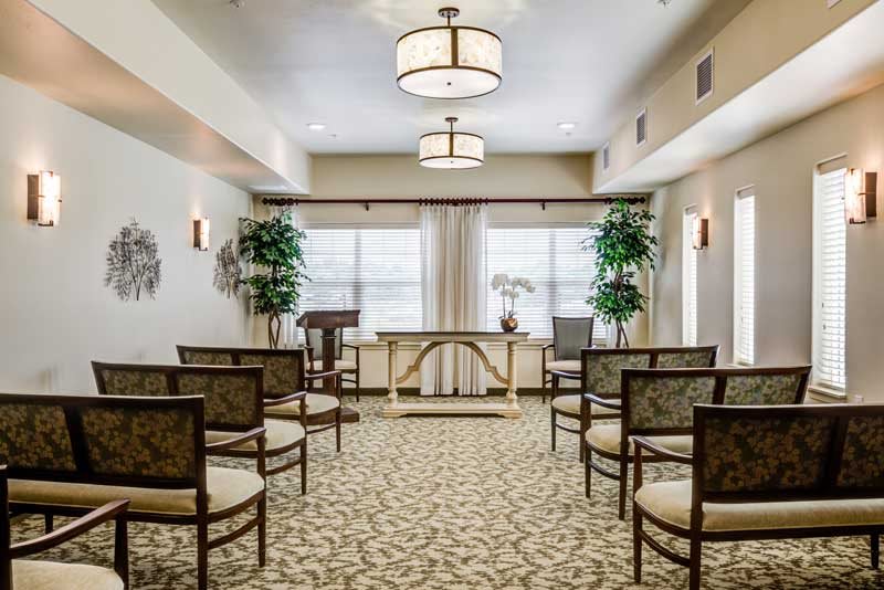A well-decorated room set up for a small ceremony with chairs arranged in rows, a central table, and decorative plants.