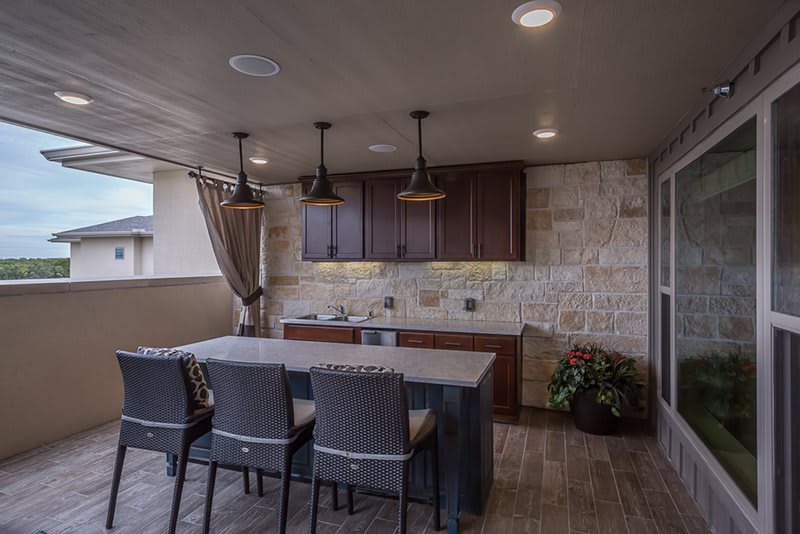 A modern outdoor kitchen with a stone wall, featuring a bar counter and pendant lighting.