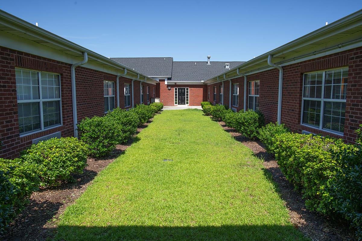 A symmetrical courtyard flanked by brick buildings with neatly trimmed grass and shrubs.