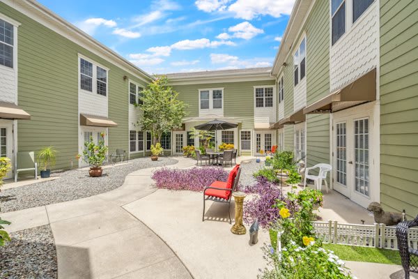 A charming courtyard with outdoor seating and colorful flowers nestled between residential buildings on a sunny day.