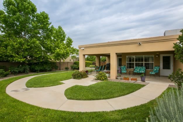 A serene backyard patio with a well-maintained lawn and surrounding trees.