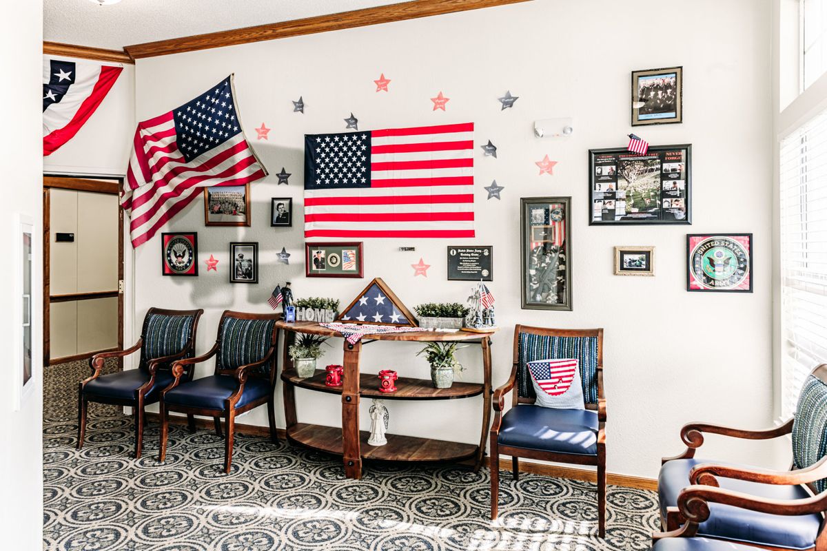 A room adorned with American flags and veteran memorabilia, featuring chairs and various framed photographs.