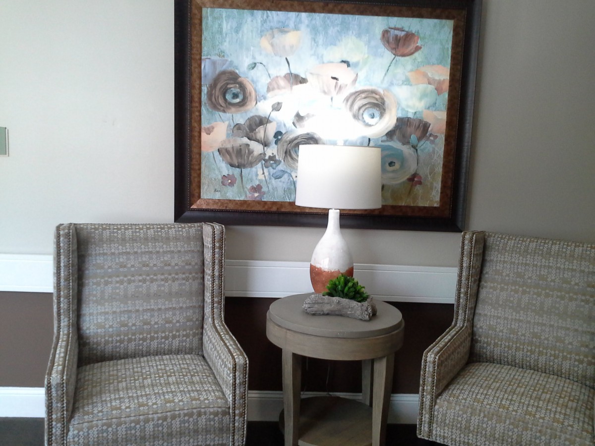 A cozy interior space featuring two upholstered chairs, a lamp on a small round table, and a large piece of artwork on the wall.