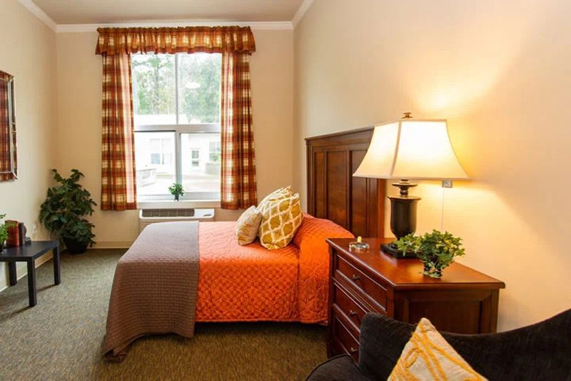 A cozy bedroom with a bed, nightstand, and lamp near a window with curtains.