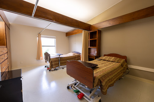 A spacious hospital patient room featuring two adjustable beds and natural light.