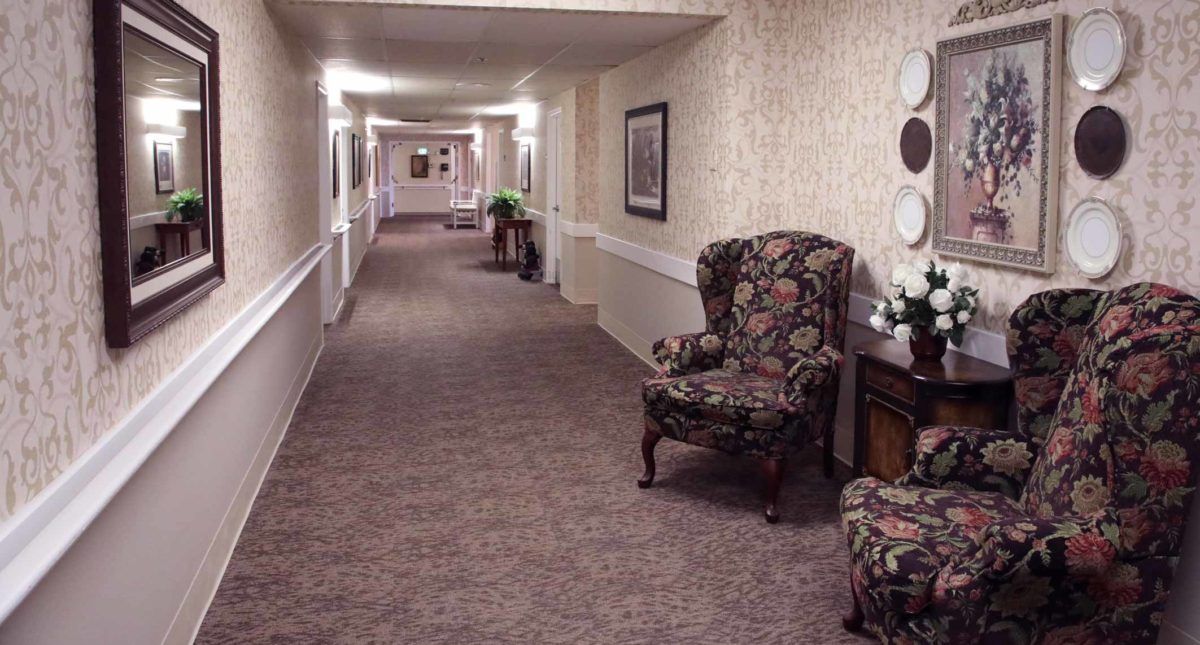 A well-lit hallway with patterned carpet, classic furniture, and decorative wall art.