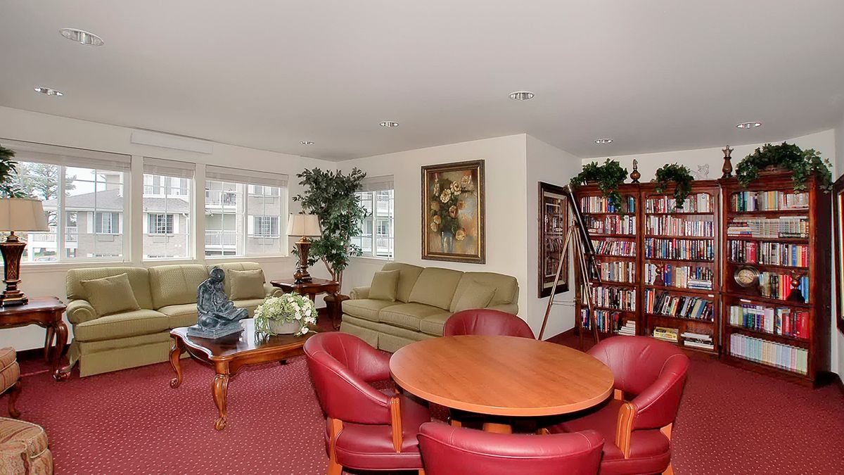 A cozy living room with comfortable seating, a wooden table, bookshelves, and potted plants.