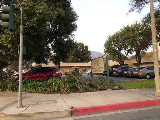 A view of a building with a sign and surrounding greenery in the parking area.
