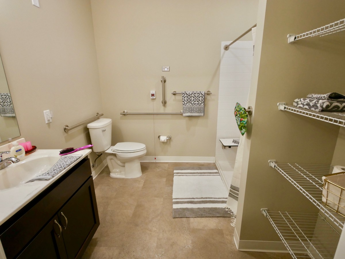 A clean and accessible bathroom with a shower, toilet, sink, and safety grab bars.