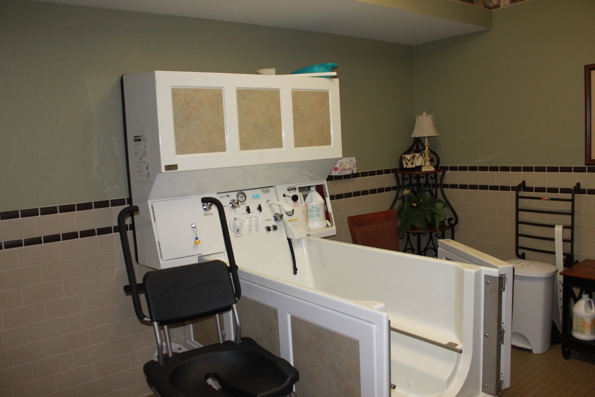 A healthcare facility room featuring a specialized bathtub with an attached chair for assisted bathing.