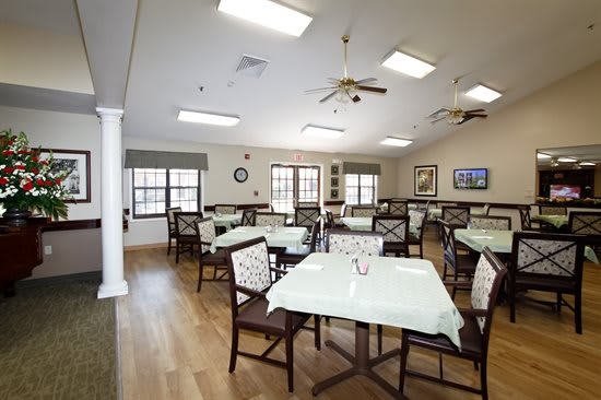 An empty dining room with neatly arranged tables and chairs, featuring wood flooring and ceiling fans.