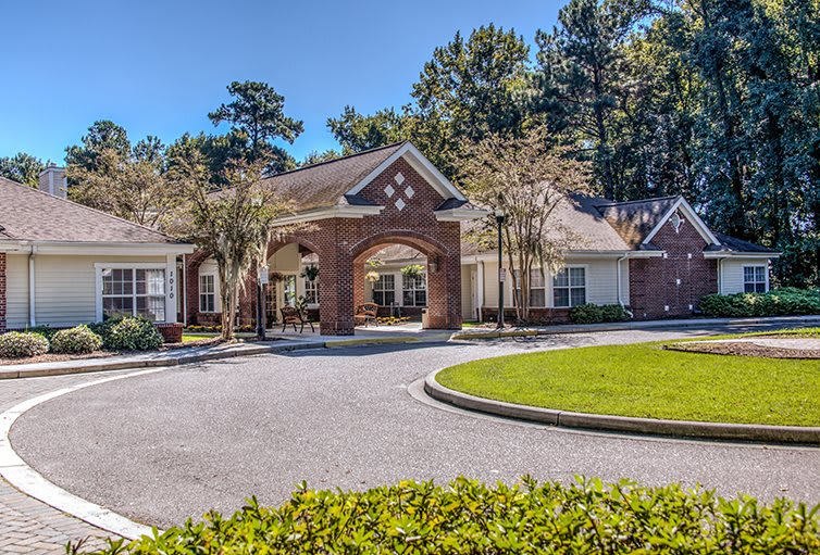 A building with a circular driveway and well-maintained landscaping, surrounded by trees under a clear blue sky.