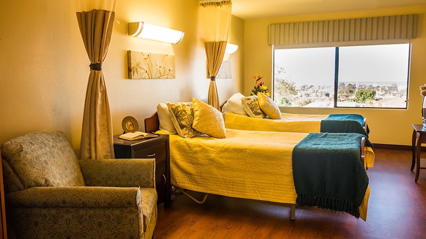 A cozy bedroom with twin beds, warm lighting, and a window offering a pleasant view.