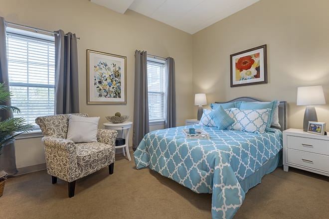 A cozy bedroom featuring a patterned bedspread, a comfortable chair, and artistic wall decor.