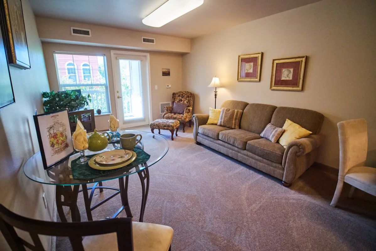 A cozy living room with a sofa, chairs, and a dining table, complemented by decorative artwork and a warm ambiance.