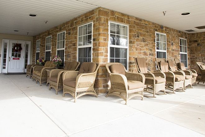 A cozy front porch with wicker chairs lined against a stone wall.